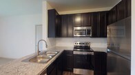 Located at 2581 Walcutt Rd in Hilliard, Ohio, this single-floor unit offers a well-designed layout with a cohesive modern aesthetic throughout. The kitchen is a standout feature, showcasing rich dark cabinetry that extends to the ceiling, granite countertops, a classic white subway tile backsplash, and a full suite of stainless steel appliances including a range, over-the-range microwave, and refrigerator. A double-basin stainless steel sink with a pull-down faucet completes the functional workspace. The kitchen opens to the main living area via a peninsula counter, creating an open and connected feel. The living space is bright and airy, with light-toned carpet, neutral white walls, and a sliding glass door fitted with vertical blinds that allows natural light to flow in. An adjacent room, accessible through an open doorway and accented by a chandelier, adds versatility to the layout. Bedrooms feature plush carpet flooring and large windows with blinds, allowing for ample natural light. The bathroom is clean and well-appointed, with dark wood-tone cabinetry, a white countertop vanity with a framed mirror, wood-look flooring, and a full soaking tub with a curved shower rod. The overall ambiance is fresh, modern, and move-in ready.