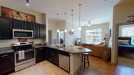 This single-story unit in College Station, Texas, offers a well-designed, open-concept layout that connects the kitchen, dining, and living areas into one cohesive space. The kitchen is a standout feature, equipped with dark espresso cabinetry, granite countertops, stainless steel appliances including a refrigerator, range, microwave, and dishwasher, and a large central island with pendant lighting overhead. The soaring ceilings in the kitchen add a sense of volume and grandeur to the space. Wood-style flooring runs throughout the main living areas, lending warmth and continuity.

The living room is bright and inviting, with large sliding glass doors providing outdoor views and abundant natural light, complemented by a ceiling fan. Multiple bedrooms offer carpeted floors, generously sized windows with exterior views, and walk-in closets with built-in shelving. Each bathroom is finished with granite-topped vanities, dark cabinetry, and wood-style flooring. The four full bathrooms ensure ample accommodation for multiple occupants. Throughout the unit, neutral wall tones, arched interior doors, and track lighting contribute to a clean, contemporary aesthetic.