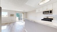 Located on Merridy Street in the Northridge neighborhood of Los Angeles, this efficiently designed single-floor unit offers a clean, contemporary aesthetic throughout. Light wood-style flooring runs continuously across the space, complementing the neutral gray walls and white trim to create a bright, cohesive atmosphere.

The open-concept kitchen and living area serves as the heart of the unit. The kitchen is well-appointed with white shaker cabinetry, a marble-style countertop, a mosaic tile backsplash, stainless steel appliances including a gas range, microwave, and dishwasher, and a peninsula that provides additional counter space and visual separation from the living area. The living area is bathed in natural light from a sliding glass door that opens onto a private balcony, offering open views of the tree-lined street below. A ceiling fan overhead adds to the room's comfort.

The bathroom features a white vanity with a stone-surface countertop, a decorative framed mirror, and hardwood-style flooring. Two closets provide practical storage throughout the unit. Additional bedrooms or flexible rooms are finished with the same light flooring, ceiling fans, wall-mounted A/C units, and windows that draw in generous natural light, contributing to the unit's airy and comfortable character.