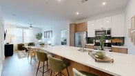 Located at 2001 Dabney Rd in Richmond, Virginia, this well-appointed 2-bedroom, 2-bathroom residence offers a thoughtfully designed single-floor layout with modern finishes and a cohesive contemporary aesthetic. The open-concept living and kitchen area serves as the heart of the home, anchored by a generous quartz-topped kitchen island with bar seating for multiple guests. The kitchen features stainless steel appliances, warm wood cabinetry contrasted by sleek white upper cabinets, a green tile backsplash, and recessed lighting overhead. Light wood-style flooring flows throughout, enhancing the bright, airy atmosphere. The living room provides a comfortable retreat with clean white walls and a ceiling fan, seamlessly connecting to the kitchen and dining area. The primary bedroom is a well-proportioned space bathed in natural light through large windows, with a barn-style sliding door adding a modern touch. The second bedroom is equally bright and inviting. Both bathrooms are finished with neutral tile flooring, wood-toned vanities, and clean white fixtures. Two closets provide ample storage. The overall design balances warm wood tones with crisp white surfaces, creating a fresh and functional living environment.