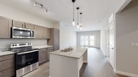 This single-story residence in Little Rock, Arkansas, offers a thoughtfully designed open-concept layout with contemporary finishes throughout. The kitchen serves as a central hub of the space, anchored by a large granite-topped island with a double-basin sink and stylish pendant lighting overhead. Taupe shaker-style cabinetry provides ample storage, complemented by granite countertops along the perimeter and a full suite of stainless steel appliances, including a refrigerator, electric range, and microwave. Wood-style plank flooring extends seamlessly from the kitchen into the adjacent living area, which is bathed in natural light from a set of glass French doors that open to the exterior. The open dining and living zones offer generous space with a neutral color palette of soft grays and warm whites, creating a clean, inviting atmosphere. The bedrooms feature the same durable wood-style flooring, ceiling fans, and windows that allow natural light in. The bathroom is finished with wood-style flooring, neutral toned walls, and a full tub and shower surround. Recessed lighting and track lighting add to the well-lit, modern character of this single-floor space.
