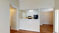 This single-floor residence offers a thoughtfully designed layout that balances functionality and comfort. The kitchen serves as a focal point of the home, featuring stainless steel appliances including a refrigerator and gas range, complemented by a sleek dishwasher. White shaker-style cabinetry lines the walls, providing generous storage space, while light granite-style countertops add a clean, bright aesthetic. A stainless steel double-basin sink is positioned along one wall, making the kitchen both practical and visually cohesive. The space is illuminated by a large skylight panel in the ceiling, flooding the kitchen with soft, diffused natural light and creating an open, airy atmosphere. Warm hardwood-style flooring runs throughout the kitchen, transitioning seamlessly into adjoining areas. A half-wall peninsula connects the kitchen to the living area, creating an open-concept feel while maintaining a defined sense of space. The living area features plush carpeting, offering a comfortable contrast to the hard flooring in the kitchen. The overall ambiance is clean, bright, and move-in ready, with a neutral color palette that lends itself well to a variety of interior styles.