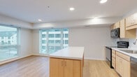 This well-appointed two-bedroom, one-bathroom unit at 2800 N Wayzata Blvd in Minneapolis offers a clean, modern aesthetic throughout. Light wood-style flooring runs continuously across the entire space, creating a cohesive and bright atmosphere. The open-concept kitchen and living area serves as the heart of the unit, anchored by a central island with a crisp white countertop and warm natural wood cabinetry. The kitchen is fully equipped with black appliances, including a range, microwave, dishwasher, and refrigerator, complemented by a tile backsplash and ample upper and lower cabinet storage. Recessed lighting illuminates the space efficiently. Large windows in both the living area and bedrooms flood the unit with natural light and provide views of the surrounding neighborhood. The primary bedroom is generously sized and features oversized windows on two walls, maximizing light and outdoor views. The second bedroom is a comfortable size with its own window and closet access. Four closets throughout the unit provide excellent storage options. The bathroom features a light wood vanity with drawers, a mirror, and grab bars, finished with the same warm flooring. A dedicated utility room adds practical functionality to this thoughtfully designed residence.