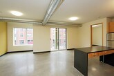 This single-floor unit presents a contemporary, industrial-inspired design characterized by polished concrete floors, bold black baseboards, and neutral cream-toned walls throughout. The open kitchen serves as a central feature, outfitted with light maple cabinetry, dark countertops, and a full suite of stainless steel appliances including a refrigerator, electric range, built-in microwave, and dishwasher. A freestanding kitchen island provides additional prep and dining space, while an exposed metal ductwork detail overhead reinforces the unit's urban aesthetic. Natural light enters the space through windows in two well-proportioned rooms, each offering views of the surrounding urban streetscape. The unit includes two bathrooms: one full bath featuring a soaking tub and shower combination with clean white surrounds, and a second bathroom with a wall-mounted mirror, dark-countered vanity, and stainless steel sink basin. The consistent use of concrete flooring, warm wood tones, and industrial accents creates a cohesive, modern ambiance throughout the entire space.