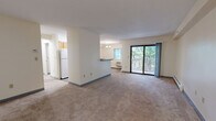 Located at 100 Queen Anne's Dr in Weymouth, MA, this well-laid-out residence offers two bedrooms and one bathroom across a single floor. The open-concept living and dining area is generously sized, featuring warm neutral carpeting, baseboard heating, and a sliding glass door that leads to a private balcony overlooking lush, tree-lined surroundings—bringing natural light and greenery into the main living space.

The kitchen is efficiently designed with warm wood cabinetry, dark countertops, light hardwood-style flooring, and a peninsula that separates it from the living area. White appliances including a refrigerator, electric range, and microwave are included. A dedicated pantry door provides additional storage within the kitchen.

The spacious primary bedroom features carpet flooring, a wall-mounted HVAC unit, a window with natural views, direct access to a walk-in closet, and a connected bathroom. The full bathroom is finished with full-height white tile surrounding a shower-tub combination, a wood vanity, and dark countertop. The second bedroom is comfortably sized with carpet, baseboard heating, and a double-door closet.

A hallway connects the main living areas to the bedrooms, and the unit includes an additional dedicated closet for extra storage. The overall aesthetic is clean, functional, and move-in ready.