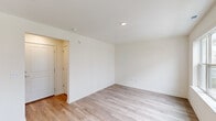 This multi-story residence spans three floors, offering a well-organized layout designed for comfortable everyday living. The ground floor serves as an entry level, providing a transitional space that connects to the upper floors via one of two staircases found throughout the home. Light hardwood-style flooring runs through the main living areas, contributing to a clean, contemporary aesthetic.

The main living level—the largest floor—houses the combined kitchen and living room, making it the social heart of the home. The kitchen is outfitted with two-tone cabinetry featuring white upper cabinets and soft sage-green lower cabinets, complemented by white quartz countertops, a center island with a built-in sink, and stainless steel appliances including a gas range, microwave, and refrigerator. A circular pendant light adds a modern accent. The open living area benefits from natural light and direct staircase access. A balcony extends the living space outdoors.

The upper floor accommodates all three bedrooms, each finished with plush carpeting and neutral walls. The primary bedroom includes a dedicated closet, while a second closet serves additional storage needs. The three bathrooms are cleanly finished with white vanities, wood-look tile flooring, and glass-enclosed walk-in showers with chrome fixtures—maintaining a consistent, modern design throughout.