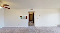 Located at 5800 Benson Dr. in Haslett, MI, this single-floor unit offers four bedrooms and two bathrooms within a well-organized layout. The living room is a standout space, featuring plush carpeting, a sliding glass door that opens to a balcony with outdoor views, and a pass-through window connecting to the kitchen — a practical design detail that enhances the sense of openness between the two areas. The galley-style kitchen is efficiently arranged with warm wood cabinetry lining both sides, ample counter space, a double sink, and white appliances including a refrigerator and range. A wood-style floor adds a clean, durable finish to this functional workspace. The four bedrooms are carpeted and well-lit, with large windows dressed in vertical blinds that allow natural light to fill each room. The spacious primary bedroom offers a generous footprint with room to spare. Two closets provide additional storage throughout the unit. The bathrooms feature wood-toned cabinetry and vinyl flooring, with one including a full tub and white tile surround. A central hallway connects the rooms with ease, and ceiling vents throughout ensure consistent climate control. The overall aesthetic is clean, neutral, and move-in ready.