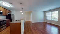This single-floor residence offers a well-designed open-concept layout that seamlessly connects the kitchen and living areas. Warm hardwood-style flooring extends throughout the main living spaces, creating a cohesive and inviting atmosphere, while the neutral color palette on the walls enhances the sense of openness.

The kitchen is equipped with stainless steel appliances, including a refrigerator, range, and over-the-range microwave. Rich wood cabinetry provides ample storage, and the granite-style countertops add a polished finish. A peninsula with pendant lighting overhead serves as a natural divider between the kitchen and the living area, offering additional counter space and casual seating potential.

The living area is generously proportioned, providing flexibility for various furniture arrangements. A hallway leads to the additional rooms, including a full bathroom featuring a wood-vanity with a solid countertop, a tub-shower combination, and light tile flooring. The bedroom is carpeted for comfort and is notably bright, with multiple windows framing views of surrounding greenery, allowing natural light to fill the space throughout the day.