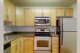 Located on the 8th floor at 4849 Connecticut Ave NW in Washington, DC, this one-bedroom unit offers a well-organized layout across a single floor. The kitchen is fully equipped with stainless steel appliances, including an electric range, over-the-range microwave, refrigerator, and dishwasher, complemented by light wood cabinetry, dark granite-style countertops, and warm hardwood-style flooring. The combined living and dining area is bright and open, with the same hardwood-style flooring extending throughout and a sliding glass door that leads to a private balcony overlooking lush treetop views. The hallway connects the main living areas to the bedroom and bathroom, with multiple closets providing generous storage throughout. The bedroom features plush carpeting, a large window with neighborhood views, and a dedicated closet with a hanging rod. The bathroom is clean and functional, featuring a tiled tub-and-shower combination, toilet, and an overhead cabinet for additional storage. Three closets throughout the unit offer practical storage solutions. The unit also includes a carpeted bedroom and a well-lit hallway entry with a pendant light fixture.