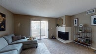 This single-floor residence offers a well-organized layout with distinct living, dining, sleeping, and kitchen areas. The living room serves as the focal point of the home, featuring plush carpeting, a white-mantled corner fireplace, and a large sliding glass door fitted with vertical blinds that allows natural light to fill the space and provides access to an outdoor area. A dining nook adjacent to the kitchen is outfitted with a ceiling fan and offers a cozy setting for everyday meals. The galley-style kitchen is equipped with dark cabinetry, granite-style countertops, a stainless steel sink, a dishwasher, and a full-size refrigerator, with wood-look flooring adding a clean, modern touch. The primary bedroom is generously sized with soft carpet, a window with curtains, and a warm, relaxed ambiance. A second bedroom provides additional flexibility and also features carpet flooring and a window with natural light. The full bathroom includes a tub-shower combination, wood-look flooring, open wall shelving, and a vanity with dark cabinetry and granite-style countertops. Textured ceilings are consistent throughout the unit, contributing to the home's classic residential character.