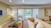 This single-floor residence offers a thoughtfully designed layout that balances comfort and functionality throughout its living spaces. The kitchen is a standout feature, outfitted with warm wood cabinetry, dark granite countertops, stainless steel appliances including a gas range, built-in microwave, dishwasher, and refrigerator, along with a peninsula that provides additional prep and casual dining space. Track lighting illuminates the kitchen, which features light tile flooring. The open living area is bright and welcoming, highlighted by large sliding glass doors that lead to a private balcony overlooking lush greenery. The living room features plush carpeting, recessed lighting, and a dedicated sitting nook with sage green accent walls. The dining area flows naturally from the living space, also carpeted and lit by recessed ceiling fixtures. The bedroom is generously sized with soft carpeting, ample natural light from large windows with sheer curtains, and spacious closets. The bathrooms are clean and well-finished — one features a full soaking tub with a decorative shower curtain and a frosted window, while the other offers an elongated vanity with wood cabinetry, tile flooring, and a large mirror. This residence combines modern finishes with a warm, livable ambiance throughout.