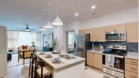 Located at 1700 Connery Ct in Garner, NC, this thoughtfully designed two-bedroom, two-bathroom residence delivers a modern aesthetic throughout its single-floor layout. The open-concept kitchen and living area serves as the heart of the home, featuring light wood shaker cabinetry, granite countertops, a deep navy tile backsplash, and a center island with an undermount sink and bar seating — all illuminated by striking conical pendant lights. Stainless steel appliances, including a refrigerator, range, and microwave, complete the well-appointed kitchen. The living room flows naturally from the kitchen, benefiting from large windows dressed with sheer linen curtains that invite generous natural light. The generously sized primary bedroom includes a ceiling fan and direct access to a closet, while the second bedroom also features multiple windows and a bright, airy feel. Both bathrooms are finished with wood-toned vanities, granite countertops, and matte black hardware; one bathroom includes a glass-enclosed walk-in shower with tile surround. Throughout the residence, light hardwood-style flooring adds warmth and continuity. A dedicated in-unit laundry closet with side-by-side front-loading washer and dryer and overhead shelving adds everyday convenience to this polished home.