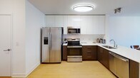 Located at One123 on 44th Street in Union City, NJ, this thoughtfully designed two-bedroom, two-bathroom residence offers a modern, clean aesthetic throughout. The open-concept kitchen is outfitted with stainless steel appliances, including a side-by-side refrigerator, electric range, and over-the-range microwave. Sleek two-tone cabinetry — white high-gloss uppers paired with warm wood-tone lower cabinets — frames crisp white countertops, creating a polished and functional cooking space. Hardwood-style flooring flows consistently through the main living areas, enhancing the sense of warmth and continuity. The living area is bright and inviting, with large windows that allow generous natural light and offer views of the surrounding neighborhood. Both bedrooms are well-proportioned, each featuring windows with natural light, closet storage, and a calm, neutral palette. The two bathrooms maintain the same modern design language, with clean white finishes, light tile flooring, wood-toned vanities with white countertops, and brushed nickel fixtures. The overall layout, as seen in the dollhouse view, is efficiently organized to maximize usable living space, making this residence a comfortable and stylish home in Union City.