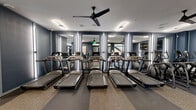 Located in Manchester, NJ, this well-appointed fitness center offers a comprehensive workout environment across a generously sized single-floor layout. The space is designed with a sleek, modern aesthetic, featuring deep navy-blue accent walls, floor-to-ceiling framed mirrors that amplify the sense of space, and vertical LED lighting strips that create a polished, professional atmosphere.

The cardio zone is equipped with a row of treadmills and elliptical machines, complemented by ceiling fans that enhance airflow and comfort during workouts. Mounted flat-screen TVs are positioned throughout for entertainment. The strength training area houses a selection of cable and resistance machines alongside a full dumbbell rack, providing a well-rounded option for weight training. Stationary cycling bikes occupy a dedicated section, ideal for low-impact cardio sessions.

Flooring throughout consists of durable rubberized material, offering both safety and comfort underfoot. Large windows allow natural light to pour in and provide views of the surrounding outdoor landscape, creating an energizing environment. Overhead, a combination of recessed lighting and modern oval pendant fixtures ensures consistent, bright illumination across the entire space. The overall design balances functionality with contemporary style, making this fitness center a practical and inviting facility.