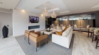 Located at 88 Cambridgepark Dr in Cambridge, MA, this elegantly designed amenity lounge offers a seamless blend of comfort and contemporary style across a single, well-appointed floor. The space is anchored by an expansive white stone kitchen island with bar seating, complemented by dark cabinetry, stainless steel appliances, a wall-mounted television, and warm pendant lighting that creates an inviting atmosphere for casual gathering and entertaining.

Adjacent to the kitchen area, a generously sized lounge features a linear fireplace set against a textured feature wall, a mounted flat-screen television, and a curated mix of plush sectional seating and leather accent chairs arranged around a central coffee table. Sculptural decorative elements and designer pendant fixtures add an artistic character to the space.

Large floor-to-ceiling windows flood the interior with natural light and offer open views of the landscaped outdoor surroundings and greenery beyond. A stone-clad column and marble reception ledge near the entry contribute a refined architectural detail that sets the tone upon arrival. Light wood-plank flooring flows throughout, unifying the distinct zones while maintaining a clean, modern aesthetic. Private booth-style seating nooks provide additional areas for more intimate conversations or focused work within this thoughtfully designed communal space.