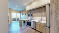 Located at 5845 Arapahoe Avenue in Boulder, Colorado, this thoughtfully designed one-bedroom, one-bathroom residence makes excellent use of its compact footprint. The open-concept layout flows seamlessly from the kitchen toward the living area, creating a sense of spaciousness throughout.

The kitchen is a standout feature, outfitted with warm wood-toned cabinetry extending to the ceiling, a neutral stone tile backsplash, stainless steel appliances including a range, microwave, dishwasher, and refrigerator, and a crisp white countertop. A built-in peninsula with pendant lighting above provides additional prep space and casual seating. Light hardwood-style flooring runs throughout, complementing the natural tones of the cabinetry. A large sliding glass door opens to a private balcony, flooding the space with natural light and offering views of the surrounding Boulder landscape.

The bedroom is carpeted for comfort, featuring a large window framing scenic mountain views, and includes a closet with sliding doors. The bathroom is finished with warm tile flooring, a wood-toned vanity with an undermount sink, and a walk-in shower with glass enclosure. Neutral wall tones and black hardware accents carry a consistent, modern aesthetic throughout the entire residence.
