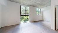 Located in Miami, FL (33136), this efficient studio unit offers a thoughtfully designed open-plan layout that maximizes every square foot. The space is defined by its striking exposed concrete ceiling, which lends an industrial-modern aesthetic throughout, complemented by large-format light tile flooring that runs seamlessly across the entire unit.

The open living area benefits from expansive black-framed windows that flood the space with natural light and frame views of lush green tree canopy outside — a refreshing contrast to the urban setting. A wall-mounted split AC unit ensures year-round comfort.

The kitchen is well-appointed with a clean two-tone design featuring warm wood lower cabinetry paired with crisp white upper cabinets. Stainless steel appliances — including a refrigerator, microwave, and dishwasher — along with a built-in cooktop and sink, make this kitchen both functional and stylish.

The bathroom is a standout feature, finished with dramatic marble-look porcelain tile surrounding the soaking tub and shower, a floating wood vanity with a white countertop, and a large mirror with overhead lighting. The entrance provides a welcoming transition into the unit via a solid grey door. Overall, the space delivers a modern, urban aesthetic with quality finishes throughout.