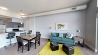 This single-floor unit at E'laan presents a contemporary design characterized by soft grey walls, wood-look flooring, and exposed ductwork that lends an urban, industrial edge throughout. The open-concept living and dining area is bright and welcoming, anchored by floor-to-ceiling sliding glass doors that lead to a private balcony offering sweeping city skyline views. Natural light flows generously into the living space, enhancing its airy, modern feel.

The galley-style kitchen is well-appointed with dark espresso cabinetry, white countertops, stainless steel appliances, and pendant lighting above an extended breakfast bar that doubles as a workspace. The layout maximizes functionality while maintaining a clean aesthetic.

The bedrooms are comfortably sized, each featuring wood-look flooring, ceiling fans or ample lighting, and large windows that bring in natural light and city views. Walk-in closet access is available in at least one bedroom. Two bathrooms serve the unit—one featuring a glass-enclosed walk-in shower and the other a full soaking tub with a shower, both finished with dark vanity cabinetry and white countertops. A dedicated in-unit laundry area with a full-size washer and dryer adds everyday convenience.