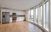 This contemporary single-floor residence is designed with clean lines and a bright, open aesthetic. The heart of the space is a well-appointed open-concept kitchen and living area, where large floor-to-ceiling windows span an entire wall, flooding the interior with natural light and offering expansive views of the surrounding urban landscape. The light hardwood flooring flows seamlessly throughout, enhancing the sense of openness and continuity.

The kitchen is thoughtfully designed with high-gloss white cabinetry extending to the ceiling, providing generous storage. A full suite of stainless steel appliances — including a refrigerator with ice maker, electric range, over-the-range microwave, and dishwasher — is complemented by a neutral tile backsplash and light countertops, creating a polished and functional cooking space. Recessed lighting illuminates the area evenly.

The bedroom features its own large window with city views, hardwood flooring, and a closet, offering a comfortable and airy retreat. The bathroom is finished with classic white subway tile surrounding a full soaking tub and shower combination, with chrome fixtures lending a clean, timeless look.

Throughout the residence, neutral walls, consistent flooring, and modern fixtures create a cohesive, contemporary ambiance well-suited to urban living.