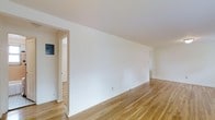 This single-floor space presents a clean and minimalist interior that is both functional and inviting. The main living area is characterized by warm-toned hardwood floors that run throughout, adding a classic and natural aesthetic to the space. The crisp white walls are smooth and well-maintained, providing a bright, neutral backdrop that enhances the sense of openness and allows for flexible interior styling.

The layout features a spacious main room with doorways leading to additional areas, suggesting a practical and connected floor plan. White baseboards frame the perimeter of the rooms, complementing the overall clean finish. An electrical panel is visible near one of the entryways, and standard wall outlets are positioned conveniently throughout.

The space benefits from even, consistent lighting that highlights the natural grain of the hardwood flooring and the clean lines of the architecture. The transition between rooms is defined by simple, white-trimmed doorways that maintain a cohesive and uncluttered look throughout. Overall, this space offers a straightforward, well-maintained environment with timeless finishes that provide a solid foundation for a variety of uses.