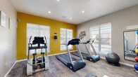 Located at 4495 Jon Cunningham Blvd in El Paso, TX, this fitness center offers a well-equipped exercise space designed to support a variety of workout routines. The room features wood-look flooring throughout, recessed lighting, and a bold yellow accent wall that adds energy to the space. Multiple windows fitted with white blinds allow generous natural light to fill the room while providing views of the surrounding area.

The cardio section is equipped with True-brand treadmills and an elliptical trainer, ideal for sustained aerobic exercise. A multi-function strength training machine and an adjustable workout bench provide options for resistance and strength training. A rack of graduated dumbbells offers additional free weight options, while accessories such as resistance bands, foam rollers, a stability ball, and medicine balls support flexibility, balance, and functional fitness. A wall-mounted television is also present for entertainment during workouts.

The room is divided into distinct functional zones, with motivational wall art enhancing the atmosphere. A pass-through window connects to an adjacent area, and posted exercise room rules ensure a considerate shared environment. The space is efficiently organized to maximize utility within its compact footprint, making it a practical and well-rounded fitness facility.