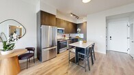 Located along Biscayne Boulevard in Miami, this well-appointed one-bedroom, one-bathroom residence offers a thoughtfully designed open floor plan with contemporary finishes throughout. Light hardwood flooring flows seamlessly across the living, dining, and kitchen areas, creating a warm and cohesive aesthetic. The kitchen is outfitted with rich dark wood cabinetry extending to the ceiling, stainless steel appliances, a white quartz countertop island with bar seating, track lighting, and a clean white tile backsplash. The open living room is bathed in natural light from floor-to-ceiling sliding glass doors that lead to a private balcony, offering expansive views of the Miami skyline and surrounding greenery. A ceiling fan enhances the airy, bright ambiance. The bedroom features large corner windows framing stunning elevated city and sky views, with direct access to a dedicated closet and an en-suite bathroom. The bathroom is finished with large-format white tiles, a glass-enclosed walk-in shower with a rain showerhead, dark hardware accents, and a floating vanity with a marble-style countertop. Additional spaces include a den, laundry area, and ample closet storage, rounding out this modern Miami residence.