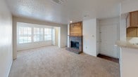 This single-story home offers a practical and comfortable layout with several notable features throughout. The living room serves as the heart of the space, highlighted by a brick fireplace with a wood-paneled accent wall rising to the ceiling and a built-in mantle shelf. Soft carpet flooring extends across the living areas, and a pass-through opening connects the living room to the kitchen, enhancing the open feel. Large windows along one wall allow natural light to brighten the space.

The galley-style kitchen is efficiently designed with white cabinetry trimmed in wood tones lining both walls, providing generous storage. Laminate countertops, a double-basin sink, electric range, dishwasher, and refrigerator are all included. Wood-look flooring runs through the kitchen, offering a contrast to the carpeted areas.

The bedroom is a well-proportioned, carpeted room featuring a ceiling fan with light fixture and windows that bring in natural light. The bathroom includes a single-sink vanity with laminate countertops, a tub/shower combination with white tile surround, and wood-look flooring. A walk-in closet is accessible directly from the bathroom. Textured ceilings are consistent throughout the home.