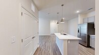 This well-appointed 2-bedroom, 2-bathroom single-floor residence offers a thoughtfully designed open-concept layout with modern finishes throughout. The combined kitchen, dining, and living area serves as the heart of the home, featuring a central island with a undermount sink, sleek white quartz countertops, and stylish pendant lighting. The kitchen is outfitted with gray shaker-style cabinetry, a white tile backsplash, and a full suite of stainless steel appliances. Wood-look luxury vinyl plank flooring extends throughout the main living areas, while a ceiling fan and access to an outdoor area enhance the living room's comfort and functionality. Both bedrooms are carpeted and feature ceiling fans and window blinds, with the primary bedroom offering a spacious walk-in closet with built-in wire shelving. The primary bathroom includes a standing shower with a glass door, while the secondary bathroom features a full tub-shower combo, both finished with brushed nickel fixtures and white vanities. Additional highlights include four closets, a dedicated pantry, an in-unit laundry area, and ample natural light throughout the space.