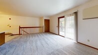 Located in Greenfield, Wisconsin, this two-bedroom, one-bathroom split-level home offers a practical and comfortable layout spread across two floors. The main living level is the heart of the home, featuring a generously sized kitchen equipped with warm honey-toned wood cabinetry, white appliances including a range, dishwasher, and refrigerator, light countertops, and durable tile-style flooring. A peninsula counter provides additional workspace and separation from the adjacent living area. The living space opens to a private balcony through a sliding glass door framed by vertical blinds, allowing natural light to filter in and offering pleasant outdoor views. A wood-railed staircase connects the levels, adding a classic architectural touch. Both bedrooms are carpeted and feature warm wood-trimmed windows with blinds that bring in natural light, along with baseboard heating. The primary bedroom is a comfortable size and is conveniently situated near the full bathroom. The bathroom includes a full tub-shower combo, a wood-vanity with storage, a toilet, and tile-style flooring. A hallway connects the upper-level rooms, completing the efficient and well-organized floor plan.