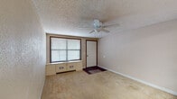 This single-floor unit presents a practical and straightforward layout across several well-defined areas. The living room serves as the welcoming entry point, featuring warm beige carpeting, neutral-toned walls, a ceiling fan with light fixture, a textured popcorn ceiling, and a large window dressed with horizontal blinds that brings in natural light. A built-in floor-to-ceiling wood shelving unit acts as a distinctive room divider, separating the living area from the kitchen while providing generous display and storage space.

The kitchen is efficiently arranged, offering light wood countertops, white upper and lower cabinetry with wood trim accents, a stainless steel sink, an electric range, a dishwasher, and a refrigerator. A skylight panel above brightens the cooking space.

The bathroom is equipped with a single-sink vanity featuring a marble-patterned countertop, a full tub-shower combination, and dark wood-style flooring that continues into the hallway areas.

A dedicated utility room houses the water heater and electrical panel, with the same dark wood-style flooring providing continuity. An additional room with light wood-style flooring and clean beige walls offers flexible use as a bedroom or secondary living space. Throughout, the unit maintains a consistent neutral color palette, delivering a cohesive and functional environment.