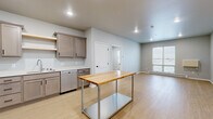 Located at 3911 20th Ave S in Fargo, ND, this thoughtfully laid-out two-bedroom, two-bathroom residence offers a comfortable and modern living environment across a single floor. The open-concept kitchen is a standout feature, outfitted with taupe shaker-style cabinetry, stainless steel appliances including a refrigerator, range, microwave, and dishwasher, complemented by open shelving and light hardwood-style flooring that flows throughout the main living areas. A butcher block-topped prep island adds both function and charm to the space. The living area is bright and inviting, with natural light filtering in through large windows. Both bedrooms are carpeted and generously proportioned, with the primary bedroom featuring a ceiling fan, a window with exterior views, and direct access to a dedicated walk-in closet outfitted with wire shelving systems. The second bedroom also includes its own walk-in closet. The primary bathroom offers a dual-sink vanity with dark cabinetry, sleek mirrors, and a full-size soaking tub, all set on light hardwood-style flooring. Throughout the unit, a neutral color palette of soft grays and whites creates a clean, contemporary aesthetic that is both welcoming and versatile.