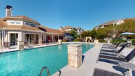This outdoor pool area in Lafayette, Louisiana offers a well-appointed resort-style retreat designed for relaxation and recreation. The centerpiece is a generously sized swimming pool with clear, turquoise water, framed by decorative stone pillar accents that add a refined architectural touch to the space. A broad concrete sun deck surrounds the pool, lined with lounge chairs ideal for sunbathing under the Louisiana sky.

Adjacent to the pool, a dedicated patio area provides shaded outdoor dining with umbrella-covered tables and chairs, set on a paved surface bordered by manicured shrubs and colorful flowering plants. Ornamental iron fencing encloses the entire area, providing security while maintaining open sightlines to the surrounding greenery and residential buildings.

A covered pavilion connects to the pool area, featuring large sliding glass doors that open directly onto the deck, allowing seamless indoor-outdoor access. The pavilion houses a convenient vending machine and is equipped with posted pool rules for guest reference. The combination of lush landscaping, stone accents, and thoughtfully arranged seating areas creates a vibrant, welcoming atmosphere well-suited for both leisure and social gatherings throughout the year.