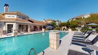 This outdoor pool area in Lafayette, Louisiana offers a well-appointed resort-style retreat designed for relaxation and recreation. The centerpiece is a generously sized swimming pool with clear, turquoise water, framed by decorative stone pillar accents that add a refined architectural touch to the space. A broad concrete sun deck surrounds the pool, lined with lounge chairs ideal for sunbathing under the Louisiana sky.

Adjacent to the pool, a dedicated patio area provides shaded outdoor dining with umbrella-covered tables and chairs, set on a paved surface bordered by manicured shrubs and colorful flowering plants. Ornamental iron fencing encloses the entire area, providing security while maintaining open sightlines to the surrounding greenery and residential buildings.

A covered pavilion connects to the pool area, featuring large sliding glass doors that open directly onto the deck, allowing seamless indoor-outdoor access. The pavilion houses a convenient vending machine and is equipped with posted pool rules for guest reference. The combination of lush landscaping, stone accents, and thoughtfully arranged seating areas creates a vibrant, welcoming atmosphere well-suited for both leisure and social gatherings throughout the year.