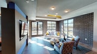Located at 2405 Marshall St in Fort Worth, Texas, this single-floor amenity space combines industrial character with contemporary design across several distinct functional areas. Exposed dark brick walls serve as a unifying architectural element throughout, paired with wood-look tile flooring and multi-level tray ceilings accented with bold yellow details that add a vibrant, modern touch.

The lounge area is bathed in natural light streaming through large steel-framed windows that offer views of mature trees and an adjacent outdoor deck, accessible through glass French doors. Comfortable seating arrangements featuring a white sofa, patterned accent chairs, and a metallic round coffee table create an inviting gathering space. The tray ceiling with recessed and flush-mount lighting adds visual depth overhead.

A dedicated game room offers a full-size pool table set against a textured stone-tile accent wall, with wood-look flooring and contemporary artwork adding personality to the space.

The conference room features a long hardwood table surrounded by modern chairs, a large wall-mounted display screen, and the same brick and steel-framed window aesthetic, making it well-suited for meetings or presentations. Together, these areas form a cohesive, well-appointed communal environment.