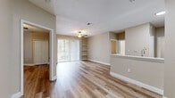 Located at 5819 Legacy Crescent Pl in Riverview, FL, this single-floor residence offers a clean, modern aesthetic throughout. Light-toned wood flooring extends across the main living and bedroom areas, creating a cohesive and airy feel. The open living room is highlighted by a ceiling fan with light fixture, built-in corner shelving, and a sliding glass door fitted with vertical blinds that fills the space with natural light and provides views of the surrounding greenery. The kitchen features white shaker-style cabinetry, light stone countertops, an undermount sink, and black appliances, including a gas range with overhead ventilation. A pass-through counter connects the kitchen to the living area, enhancing the open-concept flow. The bedrooms are well-proportioned with wood flooring, ceiling fans, vertical blinds, and closet storage. A dedicated laundry area with white cabinetry provides added convenience. The bathroom is finished with neutral tile flooring, a tiled tub-shower surround, a white vanity with mirror, and bright overhead lighting. Warm beige tones on the walls throughout lend a calm, neutral backdrop, making this a practical and well-appointed single-level home.