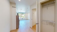 Located at 4612 Stone Way N in Seattle's Wallingford neighborhood, this modern studio unit offers a thoughtfully designed single-floor layout that maximizes every square foot. Light hardwood flooring runs throughout, complementing the clean, white-painted walls and recessed lighting that create a bright and airy atmosphere.

The open living area is a standout feature, with large windows and a set of French doors that flood the space with natural light and provide views of the surrounding tree-lined neighborhood. The French doors open directly onto a private outdoor area, offering a seamless indoor-outdoor connection.

The kitchen is efficiently arranged along one wall and is well-appointed with sleek white cabinetry extending to the ceiling for ample storage, light-toned countertops, a stainless steel refrigerator, built-in oven, cooktop, microwave, and a single-basin sink. The contemporary finishes give the kitchen a clean, functional aesthetic.

The bathroom is finished in a crisp, all-white palette and features a large walk-in shower with sliding glass doors and white subway tile, a white vanity with undermount sink, and light hardwood-style flooring that ties cohesively to the rest of the unit. Grab bars provide added accessibility. A closet with built-in shelving and hanging storage rounds out the practical amenities of this well-designed space.