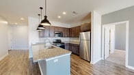 Located at 200 Jr Achievement Dr in Elkhart, Indiana, this thoughtfully designed single-floor unit offers a clean, contemporary aesthetic throughout. The open-concept kitchen is a standout feature, showcasing rich dark cabinetry, granite countertops, a subway tile backsplash, and a full suite of stainless steel appliances including a gas range, microwave, and refrigerator. A generously sized kitchen island with pendant lighting serves as both a functional workspace and a natural gathering point, flowing seamlessly into the living area. The living space is finished with wood-style plank flooring and neutral gray walls, lending a bright and airy atmosphere. French doors open to a private balcony, allowing natural light to fill the room alongside a ceiling fan that enhances comfort year-round. The bedrooms are carpeted for warmth and comfort, each equipped with ceiling fans and closets offering wire shelving for organized storage. The bathroom is well-appointed with a dark wood vanity, granite countertop, a large mirror, and a tub-shower combination. Consistent use of neutral tones, modern fixtures, and quality finishes throughout the unit creates a cohesive and inviting living environment.