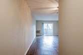 This single-floor unit offers a clean, modern aesthetic throughout, anchored by rich, dark hardwood-style flooring that runs continuously across the space. A long entry hallway with flush ceiling lighting welcomes you in, leading to an open living area bathed in natural light from a sliding glass patio door. The living room is generously proportioned, with neutral-toned walls and a wall-mounted HVAC unit, offering a versatile canvas for a variety of furniture arrangements.

The kitchen is a standout feature, showcasing white shaker-style cabinetry with contemporary hardware, gray quartz-style countertops, and a mosaic tile backsplash in neutral tones. Stainless steel appliances — including a gas range, over-the-range microwave, and refrigerator — complete the well-equipped cooking space. A window above the sink allows for natural light and ventilation.

The bedrooms are comfortably sized, each featuring the same hardwood-style flooring, neutral walls, and windows fitted with blinds for privacy and light control. The bathroom is tastefully updated with large-format gray tile in the tub surround, a decorative mosaic accent band, a white vanity with integrated sink, and a mirrored medicine cabinet, creating a cohesive and functional space.