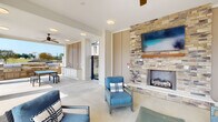 Located on Pinestone Drive in Travelers Rest, South Carolina, this single-level outdoor amenity space is thoughtfully designed to offer residents a resort-style living experience. The covered pavilion features elegant white columns with stone-accented bases that frame open views of the surrounding community and pool deck, where rows of lounge chairs invite relaxation under the South Carolina sun.

At the heart of the covered lounge area stands a dramatic floor-to-ceiling stacked stone fireplace, complete with a wood mantel and a mounted flat-screen television above, creating a comfortable gathering focal point. Blue wicker seating and coordinating accent pillows furnish the space, providing a welcoming and cohesive aesthetic throughout.

Ceiling fans are installed throughout the covered area, ensuring comfort during warm months. An outdoor kitchen and wet bar station anchor one end of the pavilion, equipped with built-in cabinetry and a sink, making it ideal for entertaining. A ping-pong table adds a recreational element to the space.

The pavilion opens directly to the expansive pool deck, where the broader residential community is visible in the background — multi-story buildings with balconies set against open skies. The overall design blends functional amenities with an inviting, community-centered atmosphere suited for year-round outdoor enjoyment.