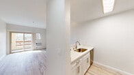This well-appointed single-floor residence offers a clean, modern aesthetic throughout, highlighted by light hardwood-style flooring that runs seamlessly across every room. The open living area serves as the centerpiece of the home, anchored by a dramatic floor-to-ceiling stacked-stone fireplace with a glass-front insert — a true standout architectural feature. A ceiling fan overhead and a sliding glass door leading to a private balcony complete the inviting atmosphere, allowing abundant natural light to fill the space.

The kitchen is thoughtfully designed with white shaker cabinetry, quartz countertops, a subway tile backsplash, a single-basin sink with a brushed gold faucet, and a full suite of stainless steel appliances including an electric range, over-the-range microwave, dishwasher, and refrigerator. A peninsula counter connects the kitchen to the living area, enhancing the open-concept flow.

The bedroom is generously sized with a large window providing natural light and a spacious closet with built-in shelving. The bathroom features a white vanity, light hardwood-style flooring, and an accessibility-friendly grab bar. A hallway connects all areas efficiently, contributing to the home's functional and airy layout.