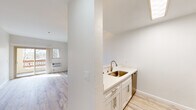 This well-appointed single-floor residence offers a clean, modern aesthetic throughout, highlighted by light hardwood-style flooring that runs seamlessly across every room. The open living area serves as the centerpiece of the home, anchored by a dramatic floor-to-ceiling stacked-stone fireplace with a glass-front insert — a true standout architectural feature. A ceiling fan overhead and a sliding glass door leading to a private balcony complete the inviting atmosphere, allowing abundant natural light to fill the space.

The kitchen is thoughtfully designed with white shaker cabinetry, quartz countertops, a subway tile backsplash, a single-basin sink with a brushed gold faucet, and a full suite of stainless steel appliances including an electric range, over-the-range microwave, dishwasher, and refrigerator. A peninsula counter connects the kitchen to the living area, enhancing the open-concept flow.

The bedroom is generously sized with a large window providing natural light and a spacious closet with built-in shelving. The bathroom features a white vanity, light hardwood-style flooring, and an accessibility-friendly grab bar. A hallway connects all areas efficiently, contributing to the home's functional and airy layout.