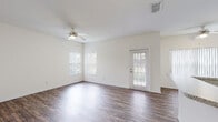 Located at 5101 SW 60th St in Ocala, Florida, this two-story residence offers a well-organized layout with a clean, neutral aesthetic throughout. The main living area is bright and open, featuring rich dark hardwood-style flooring, a ceiling fan, and multiple windows alongside a glass-paneled exterior door that allows natural light to fill the space and provides views of the surrounding greenery. A second living or flex space on the upper level mirrors this flooring and includes a distinctive half-wall detail, adding architectural interest to the room. The kitchen is thoughtfully designed with white cabinetry, light granite-style countertops, a peninsula for additional workspace, and black appliances including a refrigerator, microwave, and electric range. A bifold-door closet in the kitchen area provides convenient pantry or storage access. The bedrooms are finished with plush wall-to-wall carpeting and ceiling fans, with vertical blinds on the windows. At least one bedroom features a dedicated walk-in closet and direct access to a full bathroom. The bathroom includes a single-sink vanity with granite-style counters, white cabinetry, tile flooring, and a tub-shower combination, maintaining the home's consistent, clean design language throughout.