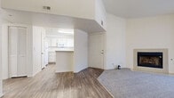 Located at 8440 Westcliff Dr in Las Vegas, NV, this one-bedroom, one-bathroom unit offers a well-organized layout across a single floor. The living room is a standout space, featuring plush carpet, vaulted ceilings, a wood-burning fireplace, and sliding glass doors with vertical blinds that allow for natural light and outdoor access. The kitchen is positioned adjacent to the living area and includes white cabinetry, a white appliance package with a gas range and built-in microwave, wood-look vinyl flooring, and a peninsula that provides additional counter space and a natural divide between the kitchen and entry area. The bedroom is generously sized, filled with natural light from a large window, and finished with soft carpet flooring. It connects directly to a spacious walk-in closet equipped with multiple built-in hanging rods for ample storage. The bathroom features wood-look flooring, a full soaking tub with tile surround, a vanity with mirror, and a clean, neutral palette. Throughout the unit, the combination of wood-look flooring in the main areas and carpet in the living and sleeping spaces provides both practicality and comfort in a bright, neutral interior.