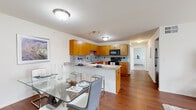 This thoughtfully designed single-floor residence offers a cohesive layout that balances functionality with modern style. The heart of the home is an open-concept kitchen and dining area, where warm honey-toned cabinetry pairs with granite countertops and a speckled tile backsplash. Black appliances, including a range, microwave, and dishwasher, are neatly integrated throughout. A peninsula with bar seating bridges the kitchen to the dining space, which accommodates a glass-top dining table set atop rich hardwood flooring. The living room continues the hardwood flooring and is bathed in natural light from a full sliding glass door that opens to an outdoor view of green grounds. The bedroom offers plush carpeting, a walk-in closet with wire shelving, and a calm, neutral palette. A secondary room with carpeted flooring, a large window, and a sliding closet door serves well as a home office or guest space. The bathroom features tile flooring, warm wood vanity cabinetry with granite countertops, and a shower-tub combination. Throughout, the space maintains a clean, contemporary aesthetic with consistent finishes that create a welcoming and practical living environment.
