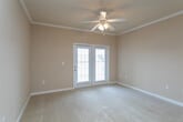 This single-story residence is designed with a practical, comfortable layout that flows naturally from room to room. Warm beige and tan tones are carried consistently throughout, creating a cohesive and inviting atmosphere. The living area is generously sized, featuring plush carpeting, crown molding, and a ceiling fan with light fixture. French doors allow abundant natural light to enter the space while providing outdoor views, enhancing the room's airy feel.

A hallway connects the living area to the private bedrooms, each of which is carpeted and equipped with a ceiling fan. The bedrooms receive natural light through blinded windows that overlook the surrounding exterior. The rooms are well-proportioned, offering functional layouts suitable for a variety of furniture arrangements.

The galley-style kitchen is outfitted with warm honey-toned wood cabinetry, granite-look countertops, a double sink, and black appliances including a refrigerator, electric range, and over-the-range microwave. Hardwood-style flooring runs the length of the kitchen, which opens toward a dining area at the far end.

The bathroom features a full soaking tub with a tiled surround, built-in shelving, and a curved shower rod, offering a clean and functional design. Throughout the residence, white baseboards and neutral walls provide a clean, move-in-ready aesthetic.