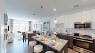 Located at Harbor Landing - Gravies Point in Glen Cove, NY, this thoughtfully designed single-floor residence offers a seamless blend of modern aesthetics and functional living. The open-concept layout connects the kitchen, dining, and living areas into one cohesive, light-filled space. The kitchen is a standout, outfitted with high-gloss white upper cabinetry, dark wood-toned lower cabinets, white subway tile backsplash, stainless steel appliances including a gas range, microwave, dishwasher, and refrigerator, and a large island with pendant lighting that doubles as a casual dining and entertaining hub. The living room is bright and airy, benefiting from oversized windows that invite abundant natural light and offer pleasant outdoor views. Light hardwood-style flooring flows throughout, tying the spaces together with warmth and continuity. The bedroom is a serene retreat featuring large windows with sheer drapery, direct access to a dedicated walk-in closet, and a private en-suite bathroom. The bathroom is finished with neutral tile flooring, clean white walls, and a tub-shower combination. The overall ambiance of the residence is contemporary and refined, characterized by a crisp, neutral palette that creates a calm and welcoming atmosphere throughout.