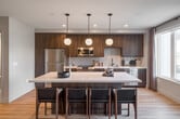Located at 3988 E Hardy St in Inglewood, CA, this contemporary two-floor residence showcases modern design throughout its well-appointed interiors. The open-concept main living area seamlessly connects the kitchen, dining, and living spaces, all finished with warm light wood flooring that runs consistently throughout.

The kitchen is a standout feature, equipped with rich dark wood cabinetry, stainless steel appliances, a light tile backsplash, matte black fixtures, and a generous central island with a white quartz countertop illuminated by a trio of globe pendant lights. Large sliding glass doors and windows flood the space with natural light while providing direct access to a balcony with open city views.

The living area offers a comfortable, well-proportioned layout with neutral walls and understated modern lighting. The bedrooms are serene and functional, with one featuring private balcony access and sweeping outdoor views. Two bathrooms serve the residence — one with a glass-enclosed walk-in shower featuring marble-style tile, and another with a soaking tub/shower combination, both finished with hexagonal mosaic tile flooring and matte black hardware throughout.