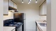This single-story residence offers a functional and straightforward layout designed for comfortable everyday living. The galley-style kitchen is efficiently organized with white cabinetry featuring wood-trim accents on both sides, black appliances including an electric range and refrigerator, a stainless steel sink, and a dishwasher. Track lighting overhead ensures the workspace is well-illuminated. The kitchen opens toward a dining and living area through a pass-through counter, creating a connected feel between the two spaces. The living area features a ceiling fan with integrated lighting and tile-style flooring, while a sliding glass door provides direct access to an outdoor greenspace, bringing in natural light and views of surrounding trees and lawn.

Bedrooms are carpeted and bright, each featuring windows with blinds that offer outdoor views. Closets with wood-panel doors and built-in shelving and hanging rods provide practical storage. The hallway connecting the rooms is carpeted as well, with a window at the far end drawing in additional natural light. The bathroom includes a full tub-shower combination with a built-in shelf. A dedicated laundry area accommodates a full-size washer and dryer, adding everyday convenience to the home.