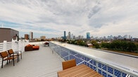 Located at 435 Melnea Cass Blvd in Boston's Roxbury neighborhood, this rooftop terrace offers a compelling outdoor space defined by sweeping, unobstructed views of the Boston skyline. The terrace is finished with light gray composite decking that extends generously across the roofline, providing a clean, low-maintenance surface suited for year-round use.

A notable sustainable feature of the space is the extensive array of solar panels integrated along the perimeter and adjacent roof sections, reflecting a commitment to energy efficiency. Galvanized metal railings line the edges of the deck, ensuring safety while maintaining clear sightlines to the cityscape beyond.

The terrace is furnished with multiple outdoor seating arrangements, including a dining table with chairs and lounge-style seating with an upholstered ottoman, making the space functional for both casual gatherings and al fresco dining. White horizontal-slat privacy fencing delineates portions of the rooftop, adding architectural character and a degree of separation between zones.

Access to the rooftop is provided through a commercial-grade push-bar door, and wall-mounted lighting ensures the space is usable after dark. The combination of panoramic Boston skyline views, sustainable infrastructure, and thoughtfully arranged outdoor furnishings makes this rooftop terrace a distinctive and practical urban outdoor space.