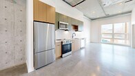 Located at 660 S 400 W in Salt Lake City, Utah, this one-bedroom, one-bathroom unit offers a thoughtfully designed industrial-modern aesthetic throughout. Polished concrete floors and exposed concrete ceilings with visible ductwork and sprinkler piping define the space's urban character, while crisp white walls keep the atmosphere bright and contemporary.

The open-concept main living area seamlessly integrates the kitchen, dining, and living spaces into one cohesive room. The well-appointed kitchen features a full suite of stainless steel appliances—including a refrigerator, electric range, microwave, and dishwasher—paired with two-tone cabinetry in natural wood and muted green tones, light quartz countertops, and a white subway tile backsplash. Large windows in the living area invite abundant natural light and provide views of the surrounding neighborhood.

The bedroom is accessed via a sleek sliding door and offers a comfortable, private retreat. Three closets throughout the unit provide generous storage options, each featuring rod and shelf systems. The bathroom is finished with polished concrete flooring, a soaking tub and shower with white tile surround, matte black fixtures, built-in open shelving, and a wood-accented vanity with a quartz countertop. The unit's cohesive design and efficient layout make it a compelling urban living option.